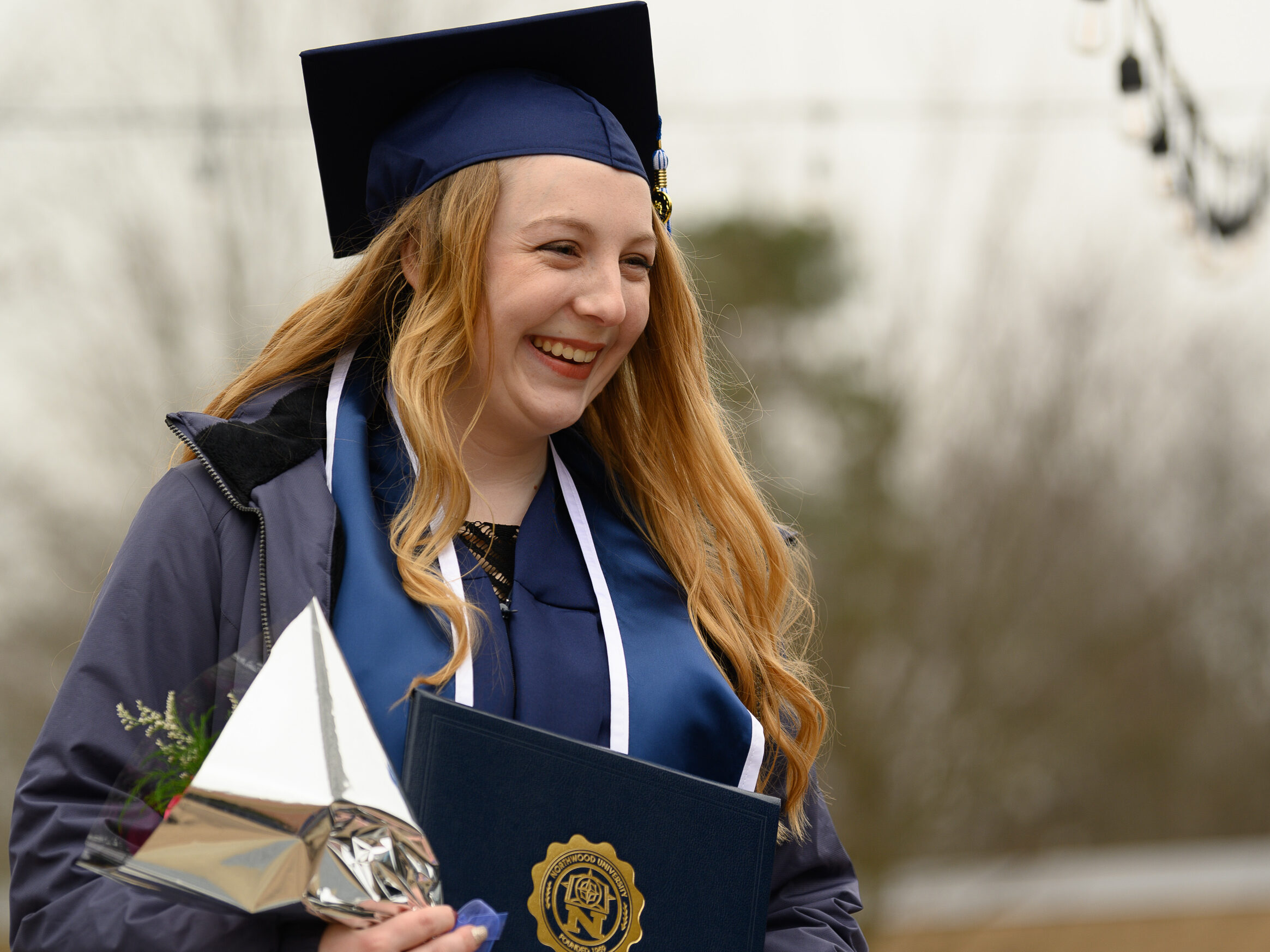 Woman smiling in cap and gown while holding flowers and her diploma