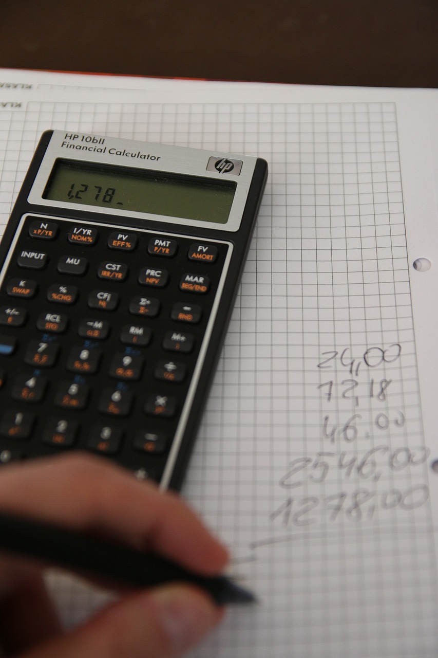 Hand holding a pen doing calculations on a paper with a calculator resting on top