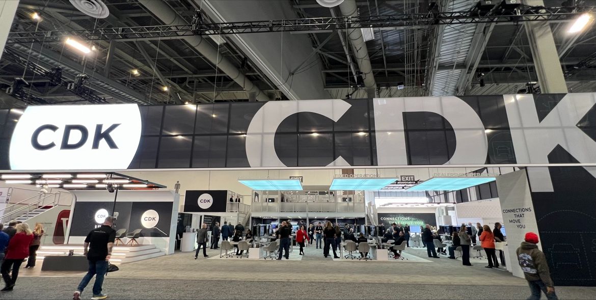 Exhibit booth with large "CDK" signage, multiple displays, and people mingling in a spacious convention hall.