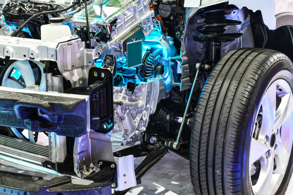 Close-up of a car’s front suspension, engine, and wheel assembly, showing exposed mechanical components and illuminated by blue accent lighting.