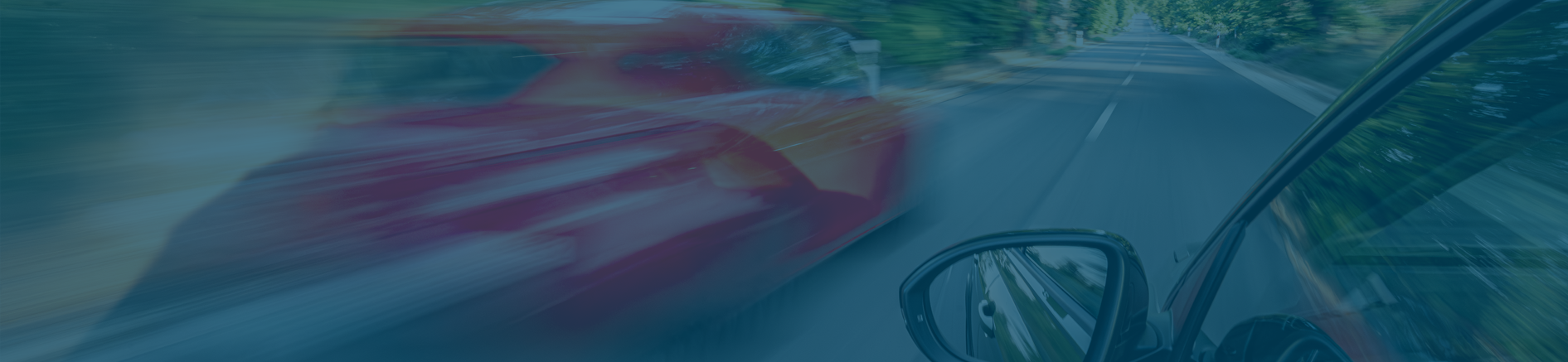 Blurred red car passing quickly on a tree-lined road, as seen from the side mirror of another moving vehicle.