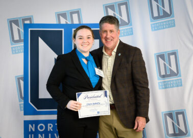 A student posing with President MacDonald, holding a certificate for the Presidential Scholarship.