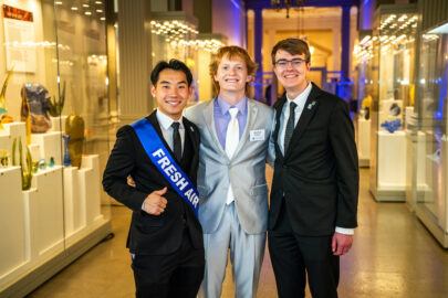 Three students pose in suits surrounded by glass walls.