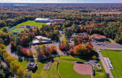 Aerial view of one of the best college campuses, showcasing sports fields, multiple buildings, parking lots, and vibrant autumn trees surrounding the school.