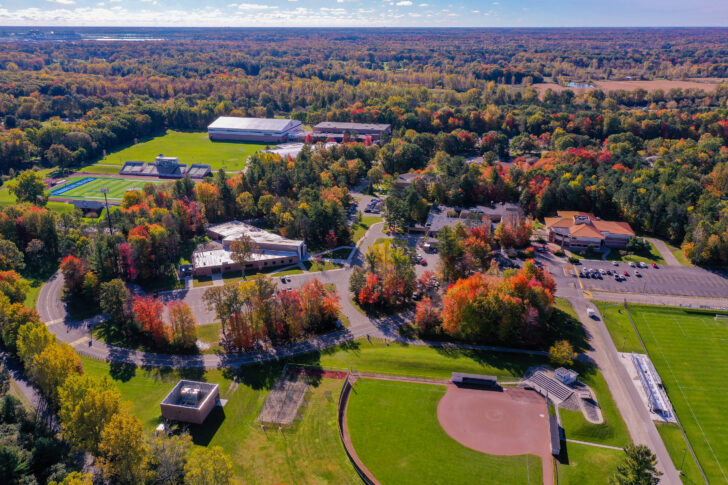 Aerial view of one of the best college campuses, showcasing sports fields, multiple buildings, parking lots, and vibrant autumn trees surrounding the school.