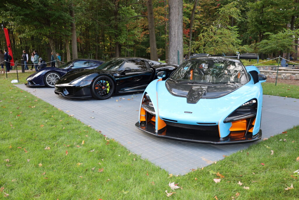 Three high-performance sports cars, including a blue and orange McLaren, are parked side by side on a paved area in a park with trees and grass—a perfect scene for motorsports jobs enthusiasts.