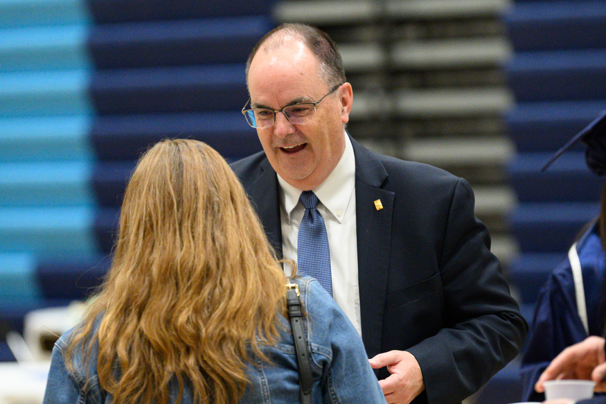 A man in a suit and tie speaks with a woman in a denim jacket about Best Undergraduate Business Schools in a gymnasium setting.
