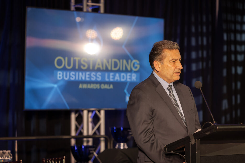 A man in a suit speaks at a podium during the Outstanding Business Leader Awards Gala, an event celebrating excellence and hosted by one of the Best Undergraduate Business Schools.
