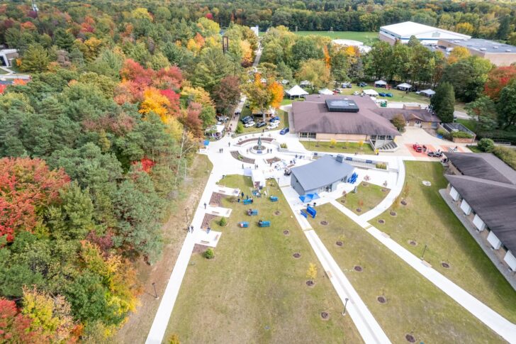 Aerial view of a campus courtyard at one of the universities in Michigan, with walkways, several buildings, scattered benches, and surrounding trees showing autumn foliage.