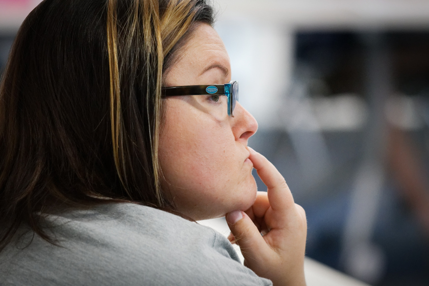A woman with glasses and highlighted hair looks thoughtful, resting her chin on her hand as she contemplates her future after earning a bachelor degree.