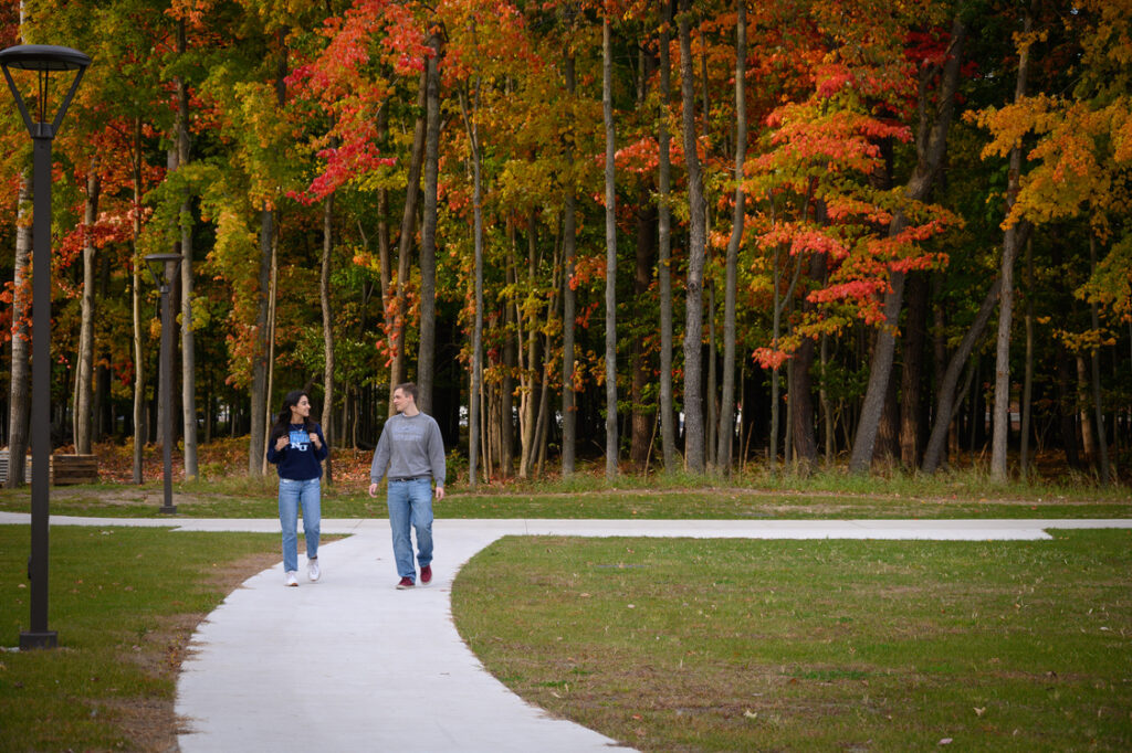 Two people walk along a curved path in a park with colorful autumn trees in the background, capturing the serene atmosphere of a university in Michigan, USA.